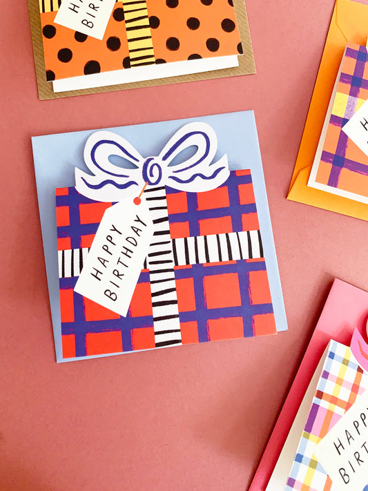 Colorful birthday cards with plaid patterns and ribbons on a pink background