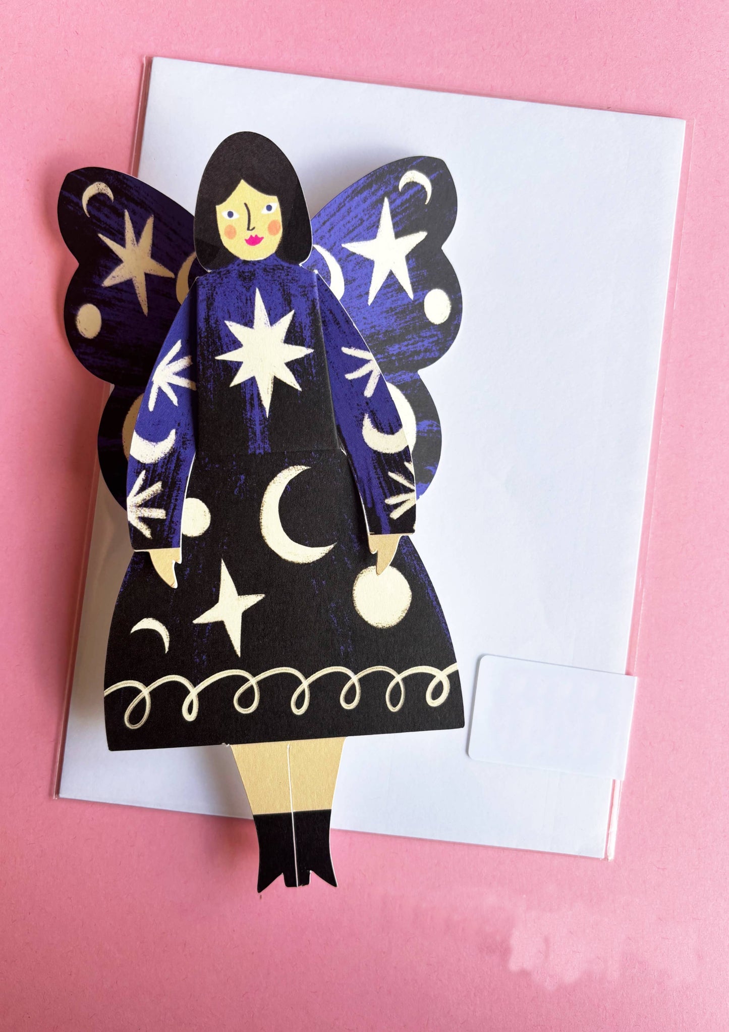 Paper cutout of a fairy with star and moon designs on a pink background