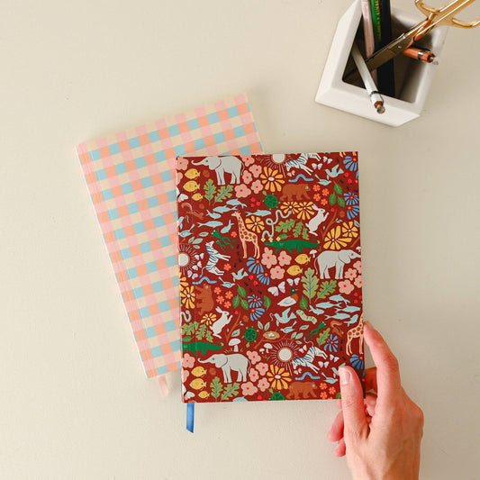 Hand holding a notebook with a colorful animal pattern on a light background