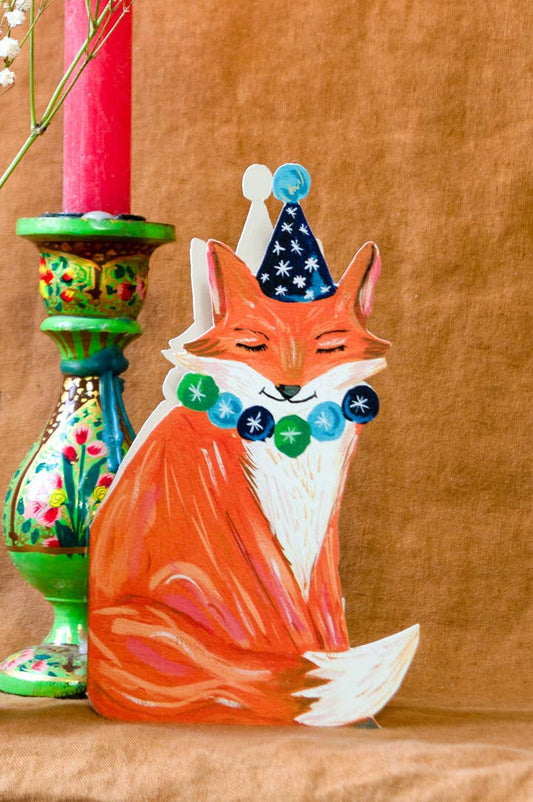 Decorative fox figurine with a party hat on a brown background