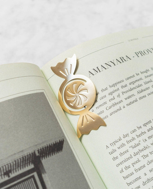 A gold metal book bookmark shaped like a wrapped candy with a spiral center, resting on an open book page.
