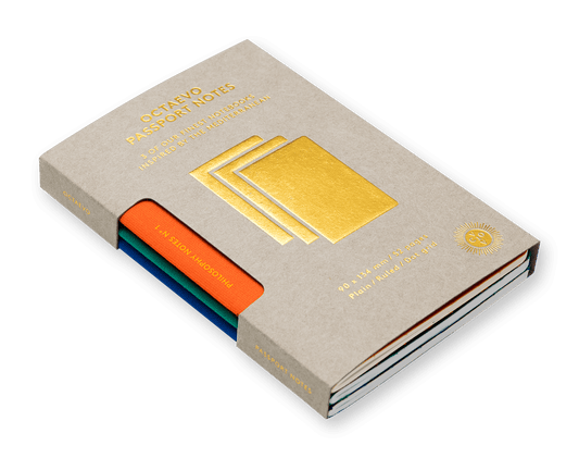 A stack of Scheido passport notes in a textured beige paper sleeve with gold foil lettering and a gold stack graphic, with colored tabs in orange, teal, and blue visible on the left, set against a solid dark green background.