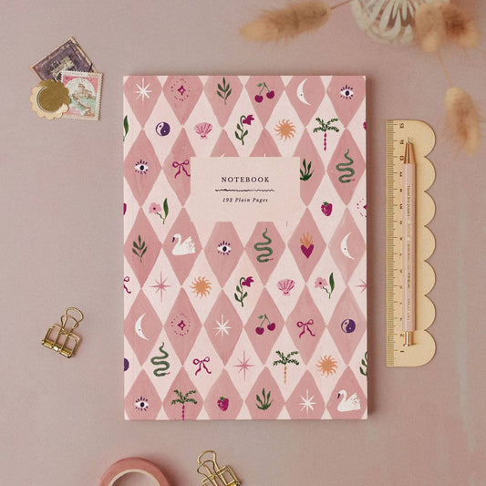 Notebook with decorative cover on a pink background with stationery items.