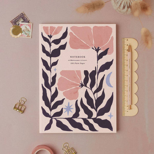 Notebook with floral design on a pink background with stationery items.
