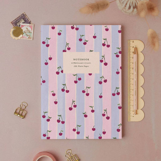 Notebook with cherry pattern on a pink background with stationery items.