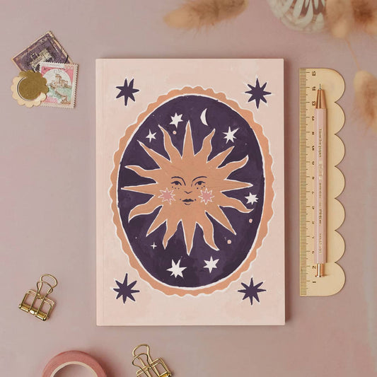 Notebook with celestial design on a pink surface with stationery items.