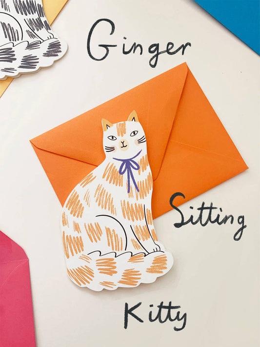 Cat-shaped paper cutout with 'Ginger Sitting Kitty' text next to orange envelopes on a light background