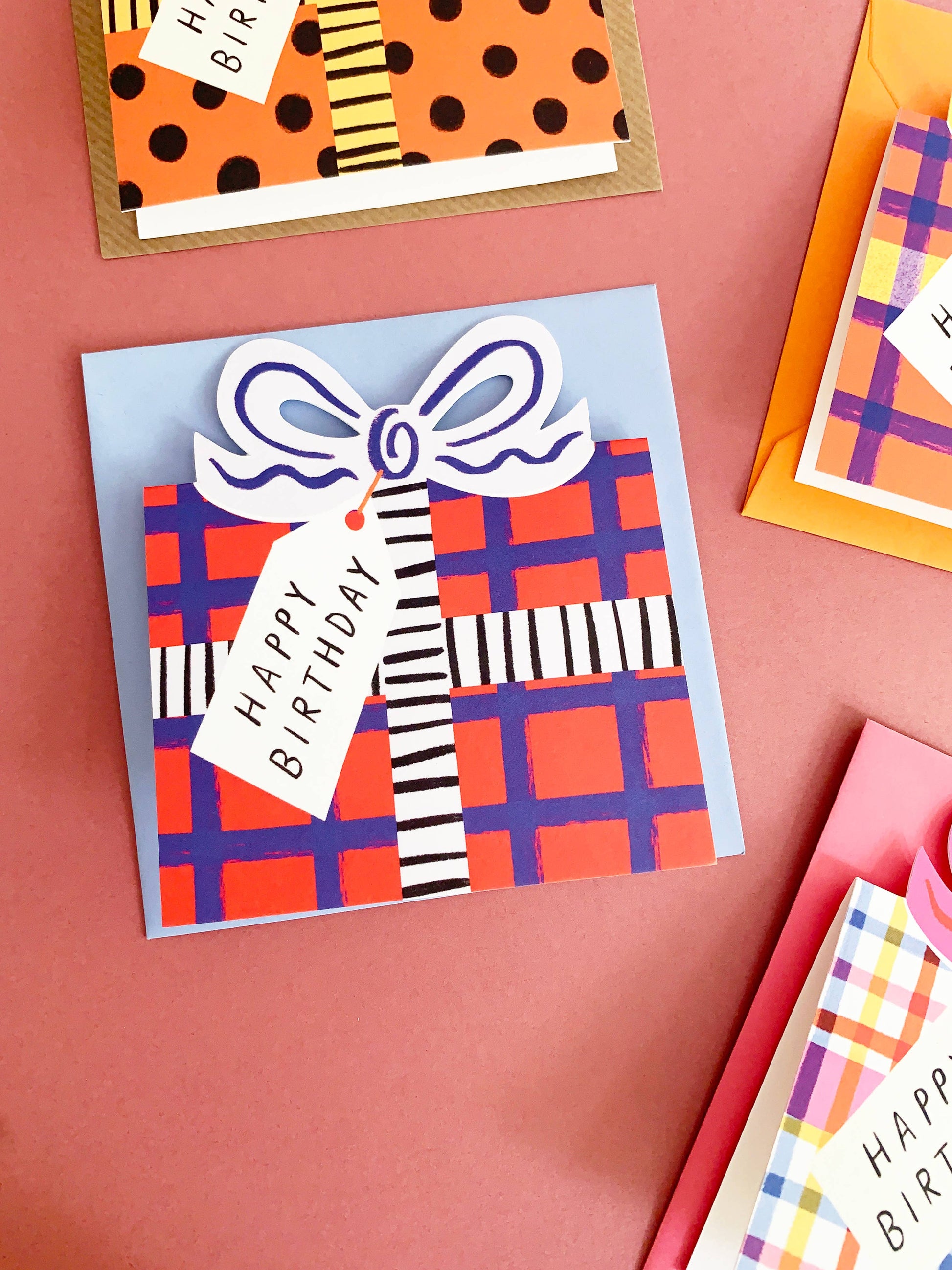 Colorful birthday cards with plaid patterns and ribbons on a pink background