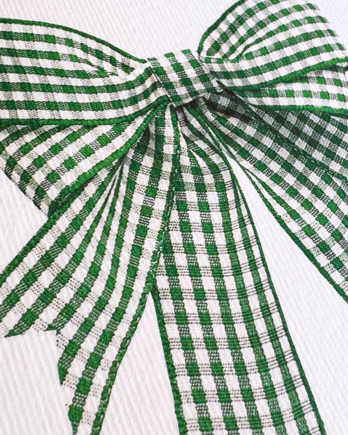 A close-up of a green and white gingham ribbon tied into a bow on a white textured background.