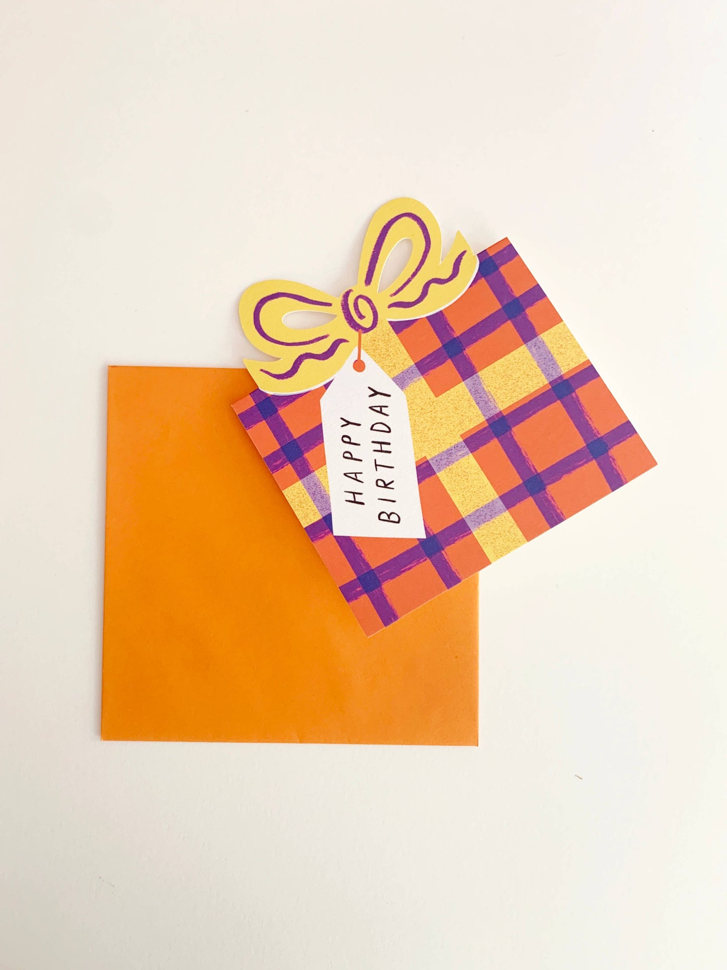 Colorful birthday card with plaid pattern and bow on an orange envelope.