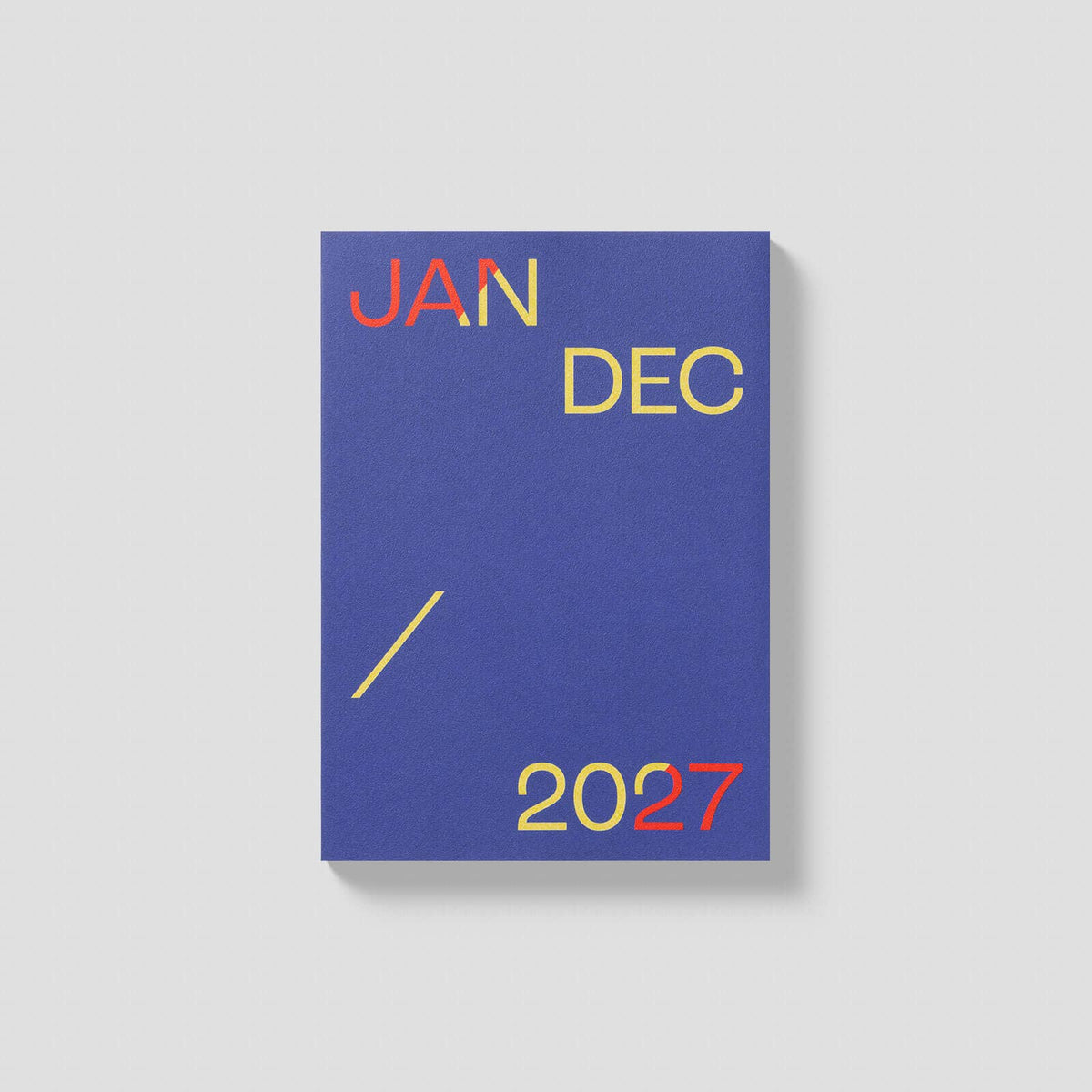 A vertical blue planner or calendar cover with the words JAN, DEC, and 2027 printed in yellow and red, shown on a light gray background.
