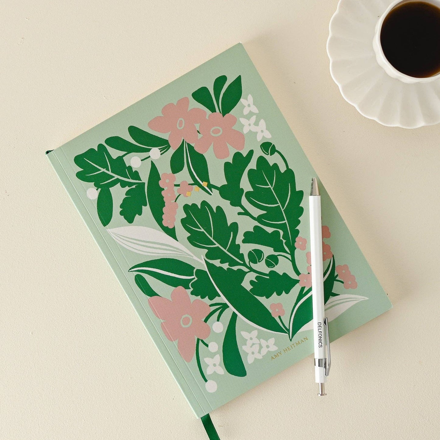 Notebook with floral design, pen, and cup of coffee on a light beige background