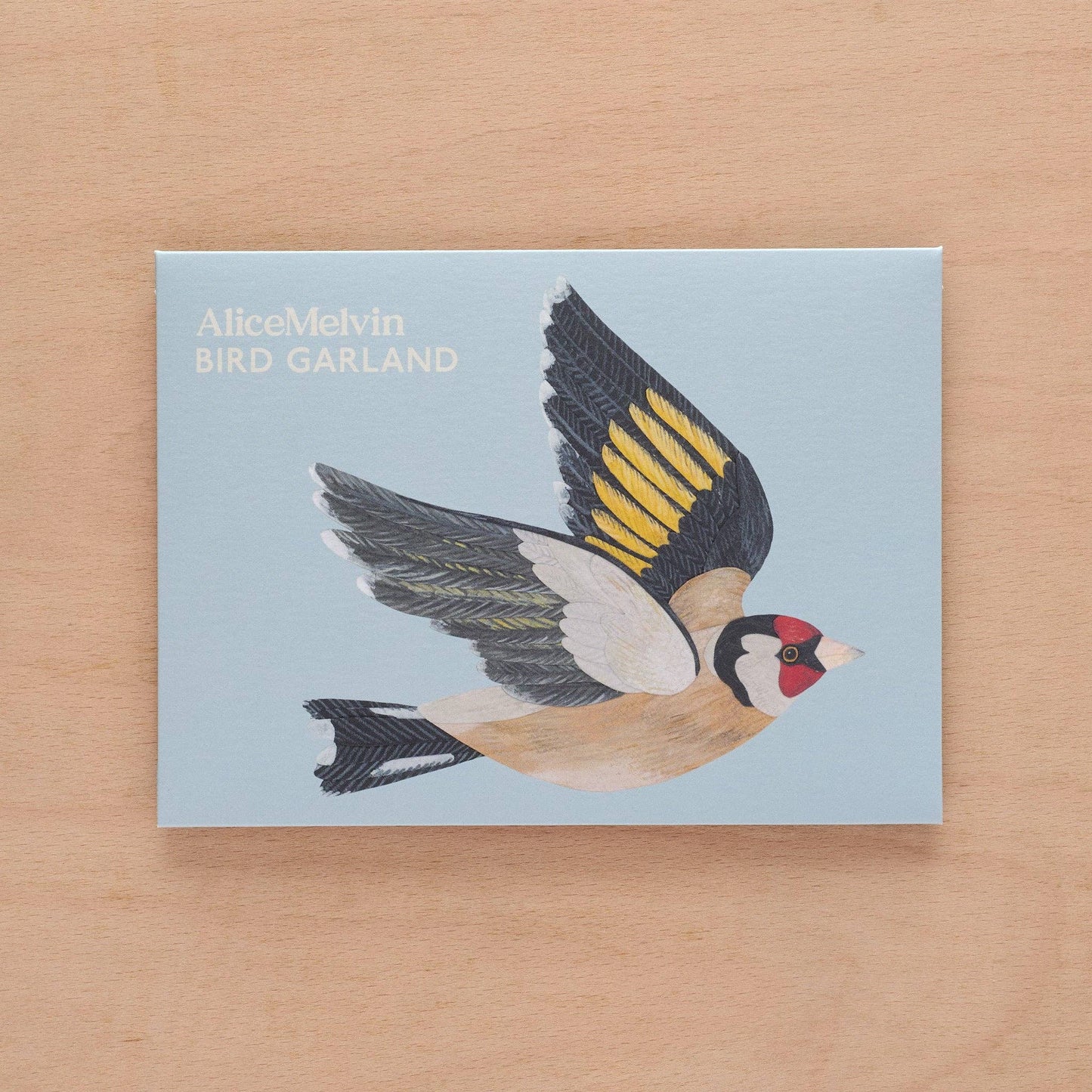 Card with a bird illustration and 'AliceMelvin BIRD GARLAND' text on a wooden surface