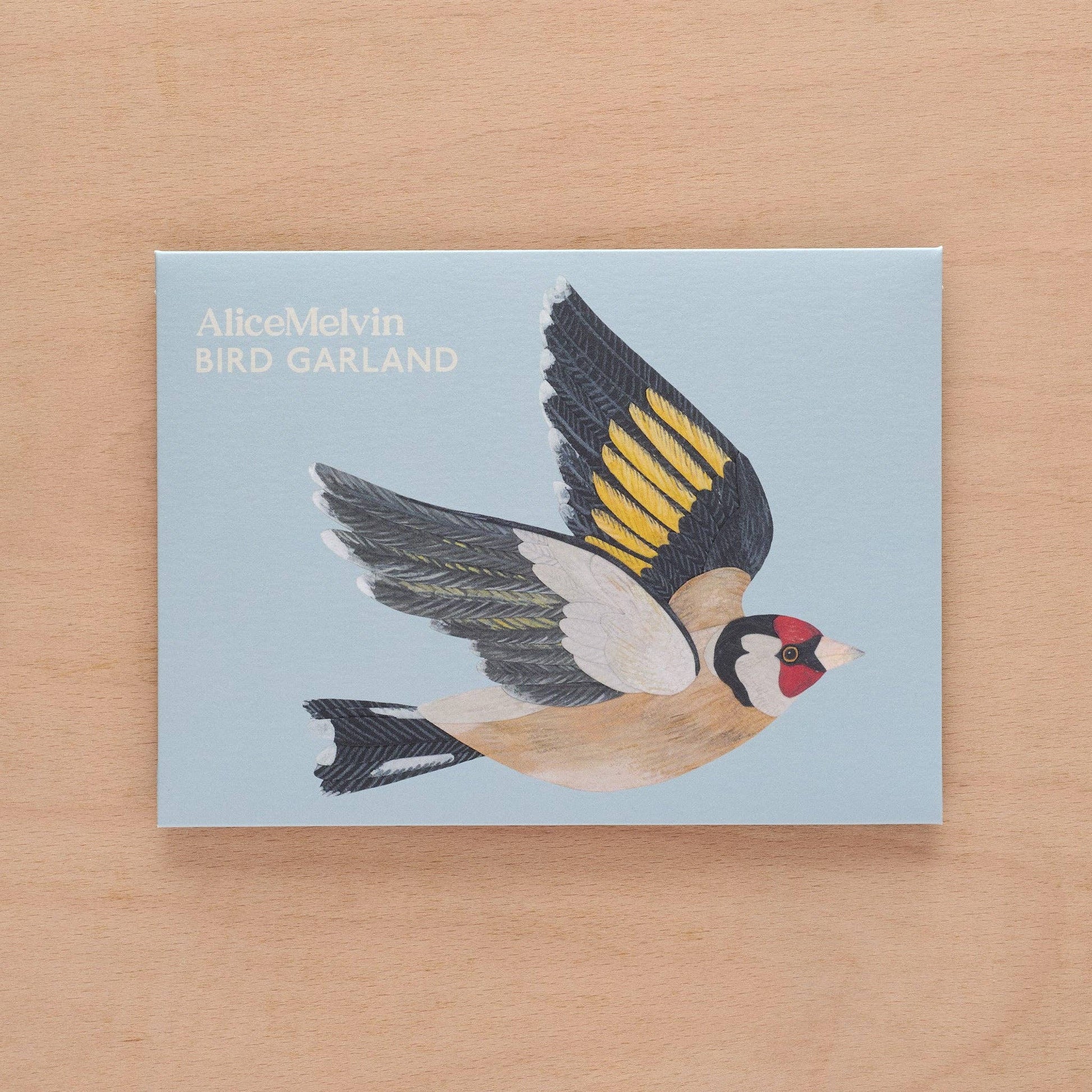 Card with a bird illustration and 'AliceMelvin BIRD GARLAND' text on a wooden surface
