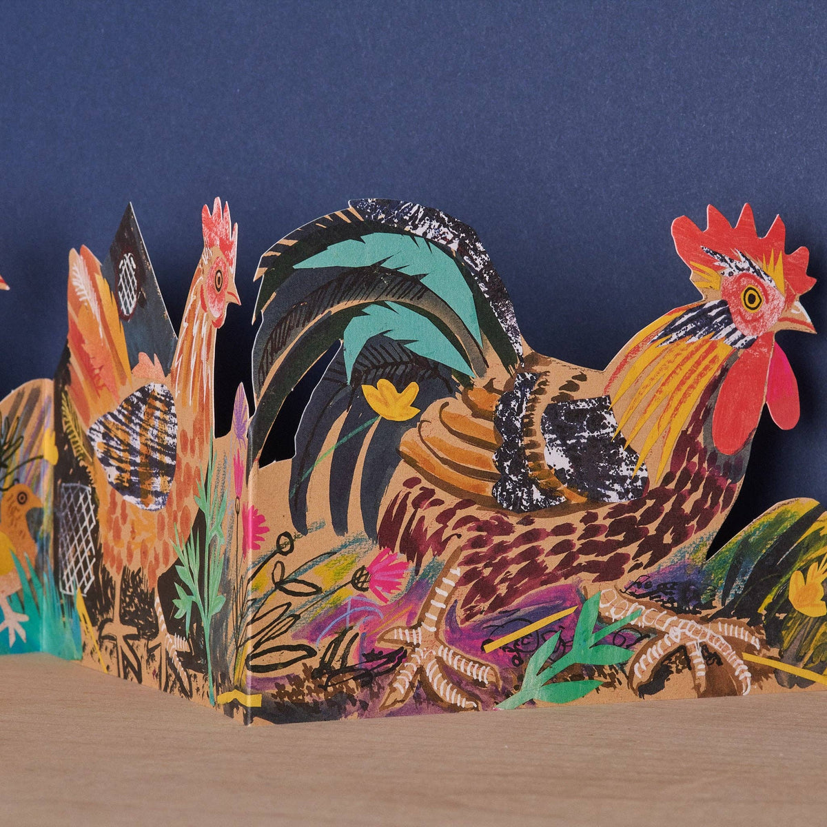 Colorful paper rooster sculpture on a wooden surface with a dark blue background