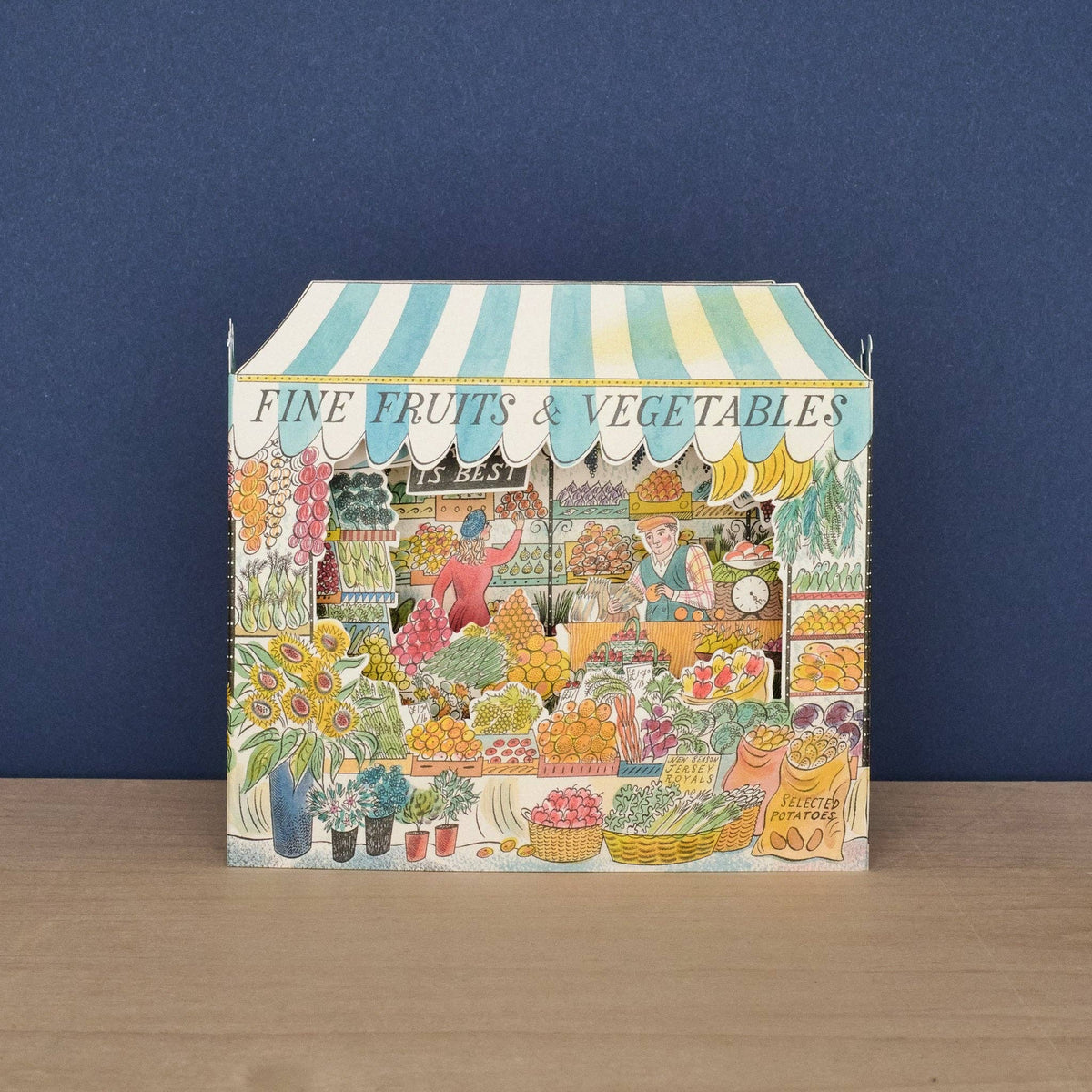 Decorative box with a market stall design featuring fruits and vegetables on a wooden surface and blue background.