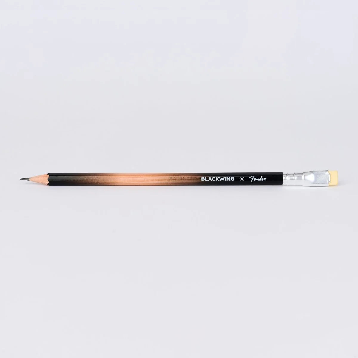 A Fender x Blackwing graphite pencil with a black-to-copper gradient barrel, shown horizontally on a light gray background.