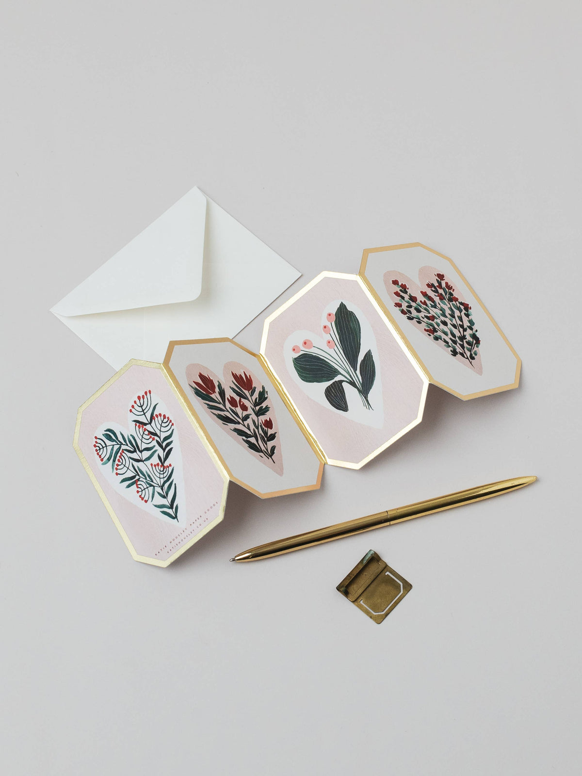 Four hexagonal cards with floral designs, a white envelope, and a gold pen on a light gray background.