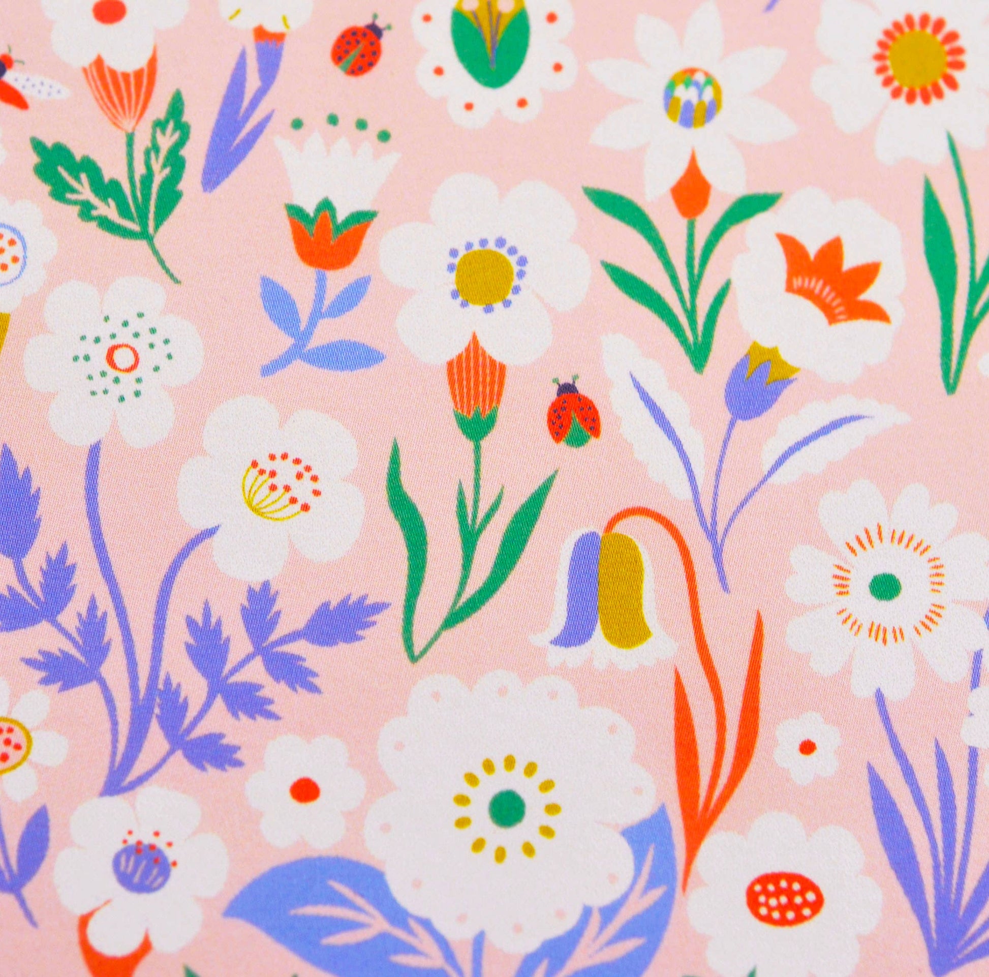 A close-up of a pink fabric or wallpaper pattern featuring a colorful floral design with white daisies, orange tulips, blue flowers, green leaves, and small ladybugs.