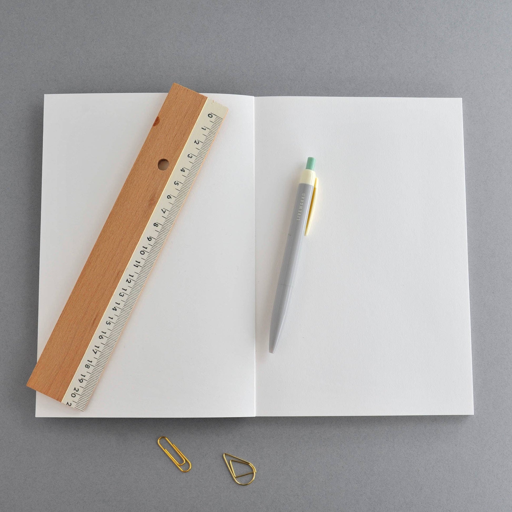 Open notebook with a ruler, pen, and paper clips on a gray background