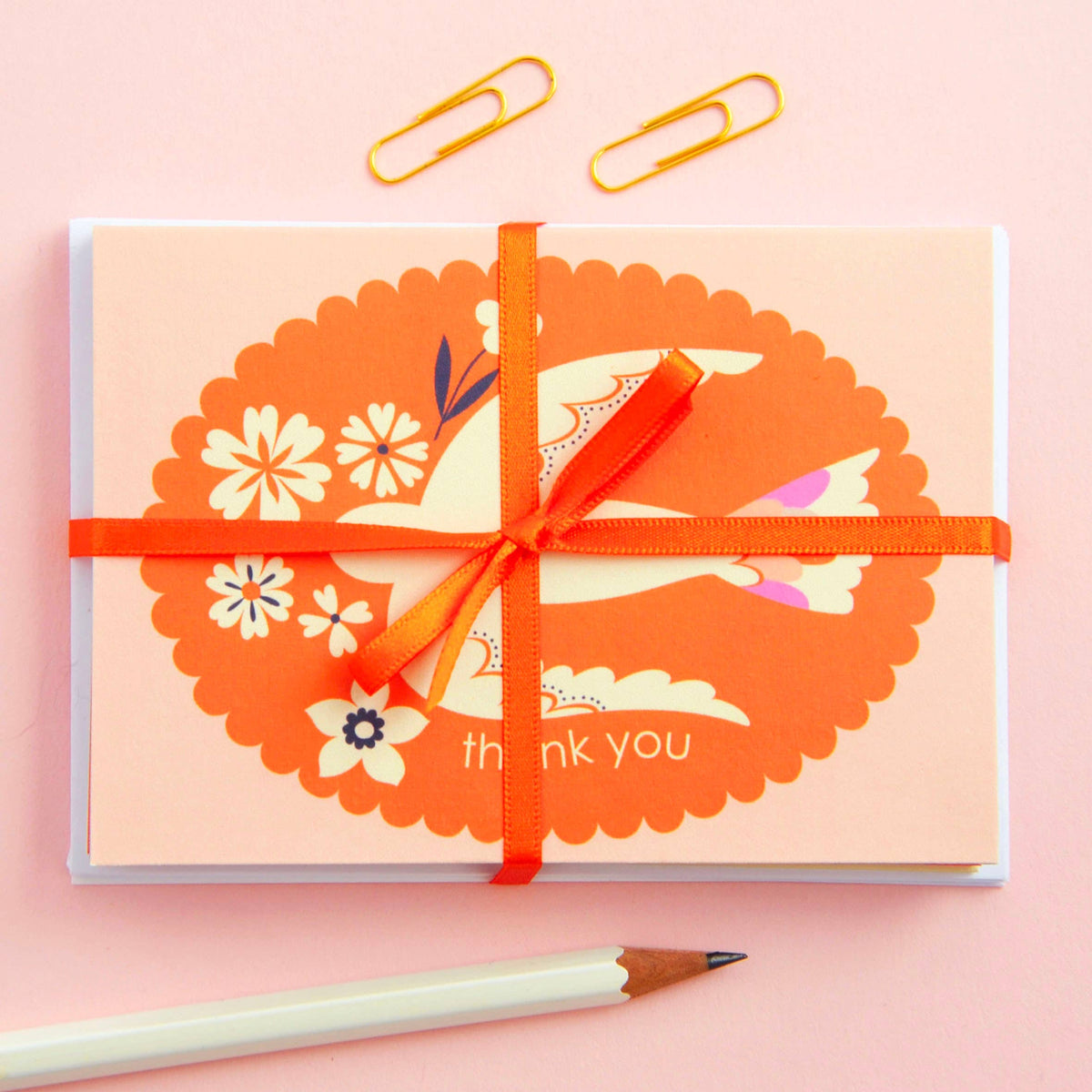 Gift card with floral design and orange ribbon on a pink background