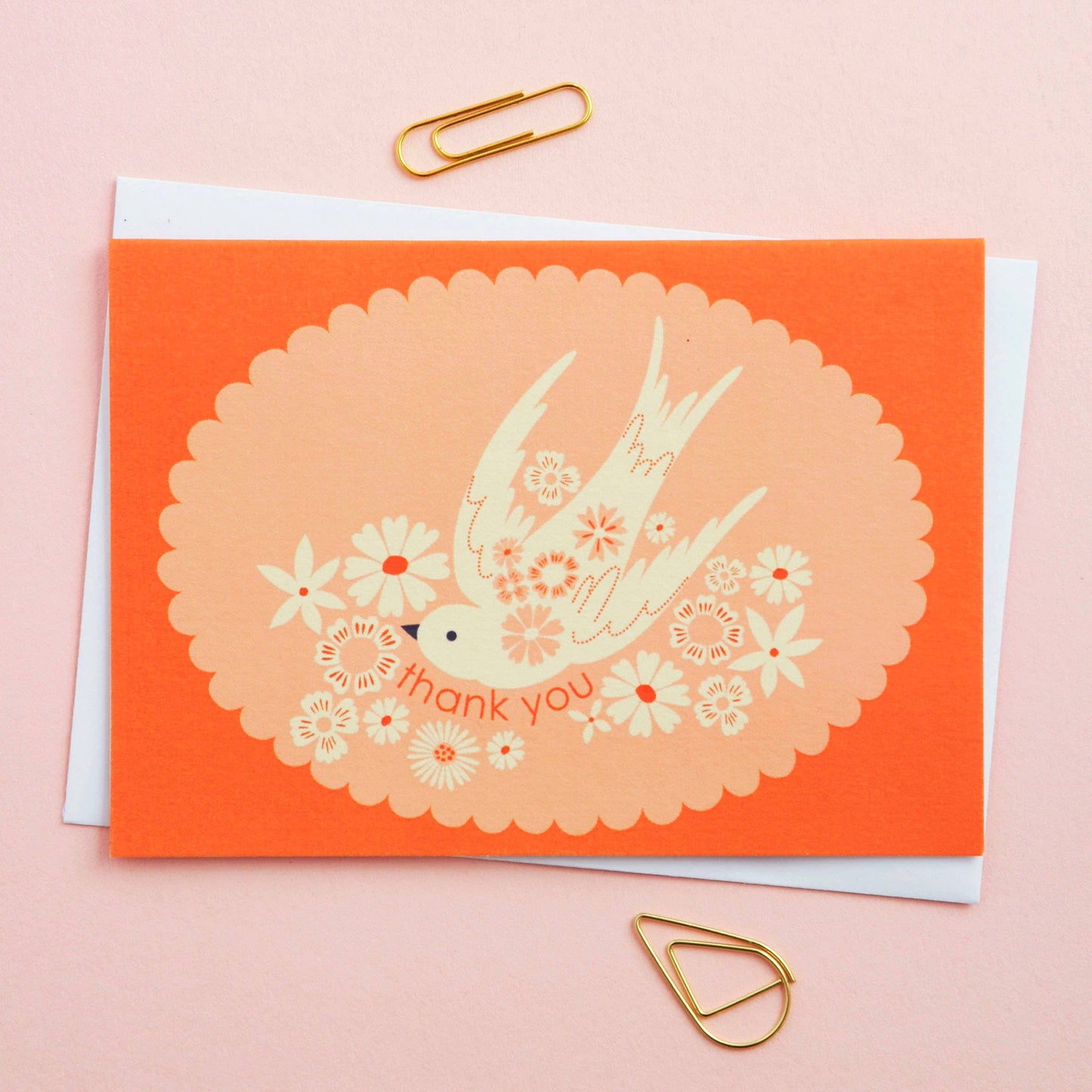 Greeting card with a bird and floral design on an orange background, featuring gold paper clips.