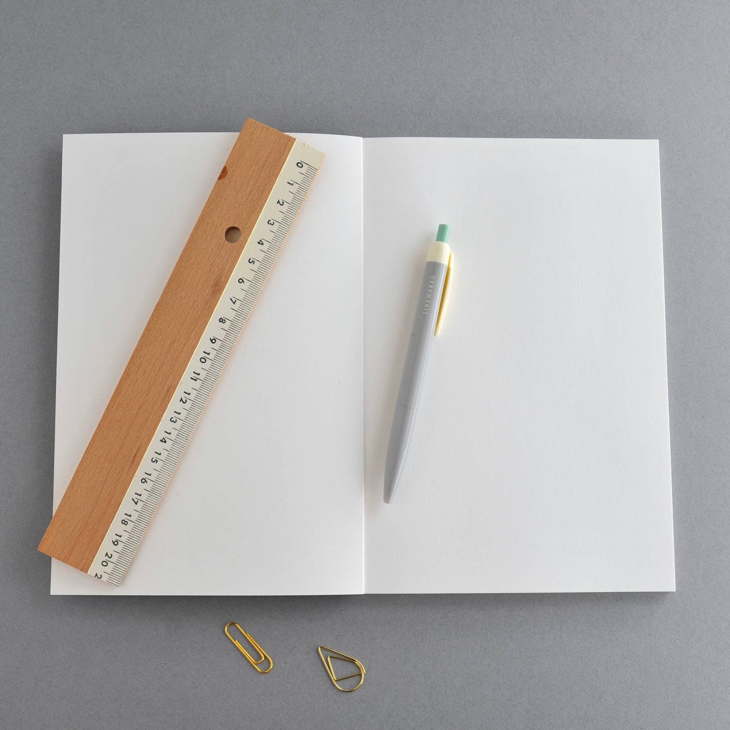 Open notebook with a ruler, pen, and paper clips on a gray background