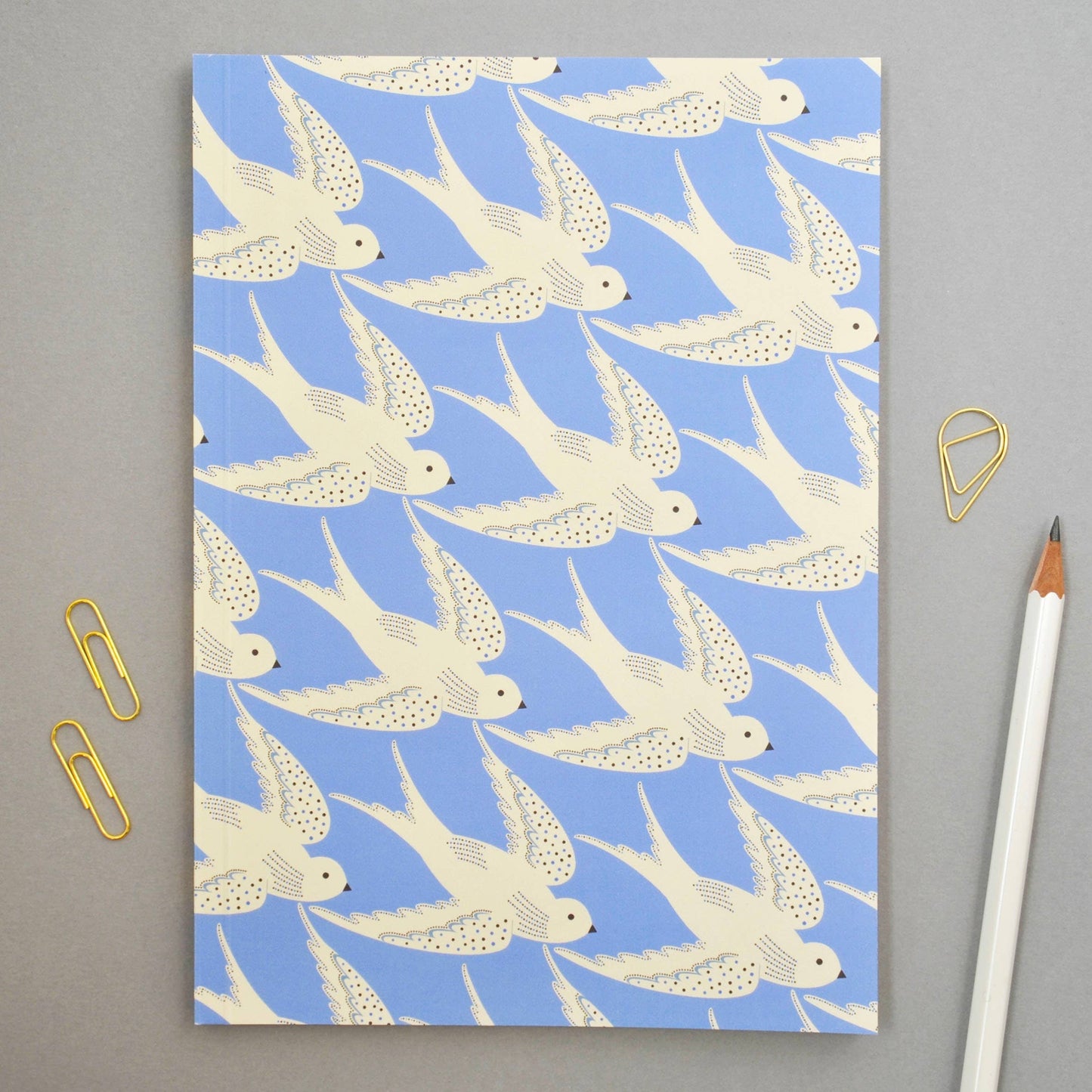 Notebook with swallow pattern on a blue background, placed on a gray surface with stationery items.
