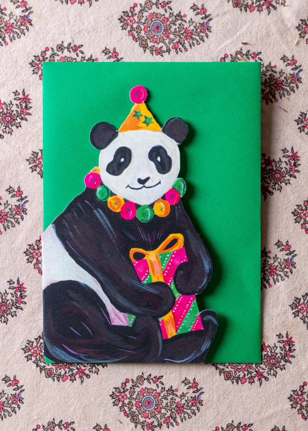 Colorful panda bear card with a green background on a patterned fabric surface