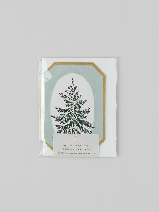 A packaged Christmas-themed folding pocket card featuring an illustrated evergreen tree inside an arched frame with a gold border on a white card, sealed in clear plastic against a light gray background.