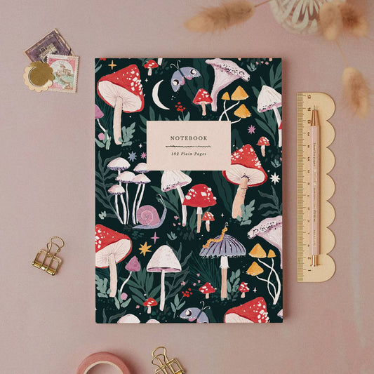 Notebook with mushroom design on a pink background with stationery items.