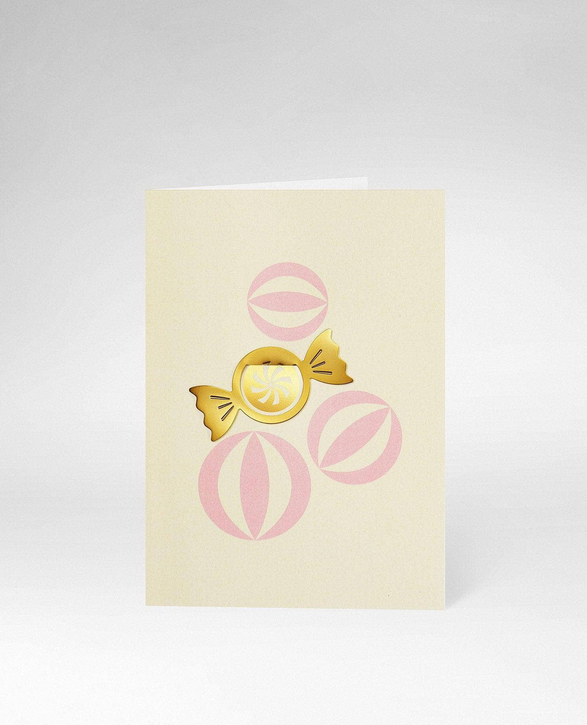 A cream-colored greeting card featuring a central gold foil candy illustration with pink circular accents, photographed on a light gray background.