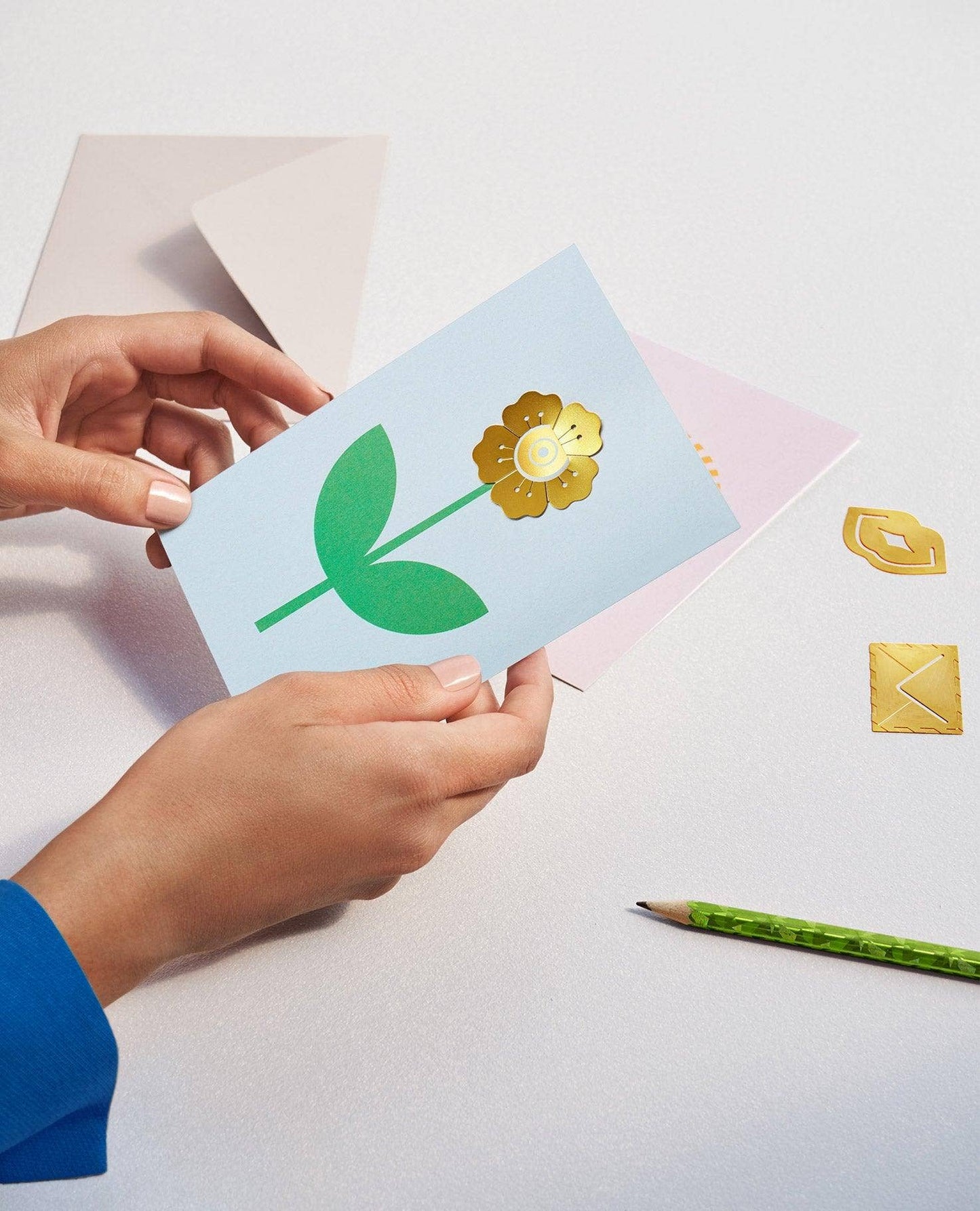 Person holding a card with a green leaf and yellow flower design on a light surface.