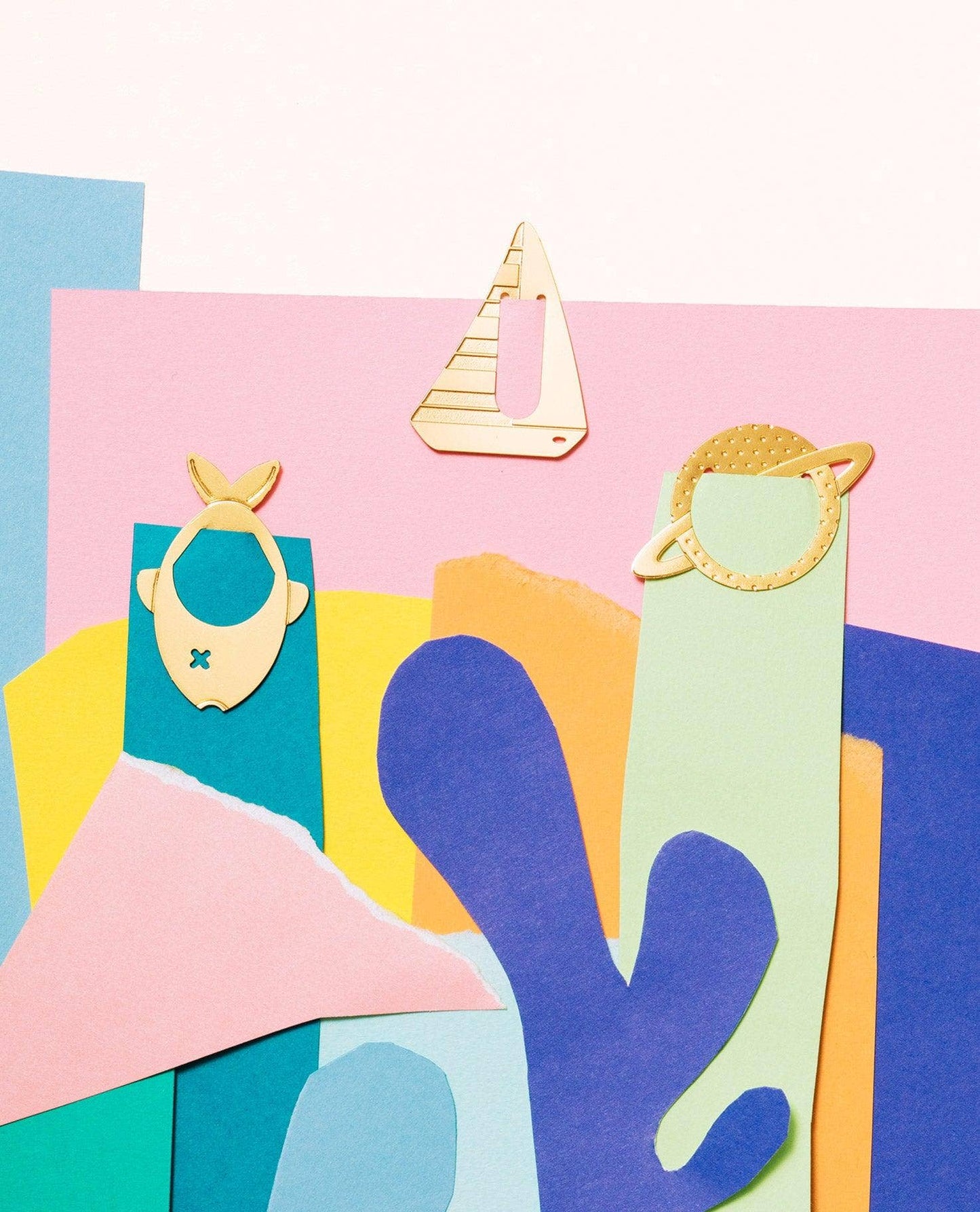A colorful abstract collage of layered paper shapes in pink, blue, teal, yellow, and purple, with three small gold-tone decorative cutout figures placed on top.