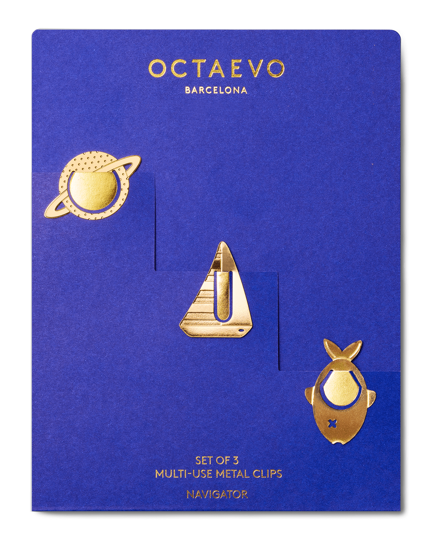 A set of three gold metal multi-use clips by Octaevo Barcelona, displayed on a blue backing card. The clips feature a planet with rings, a sailboat, and a navigator.