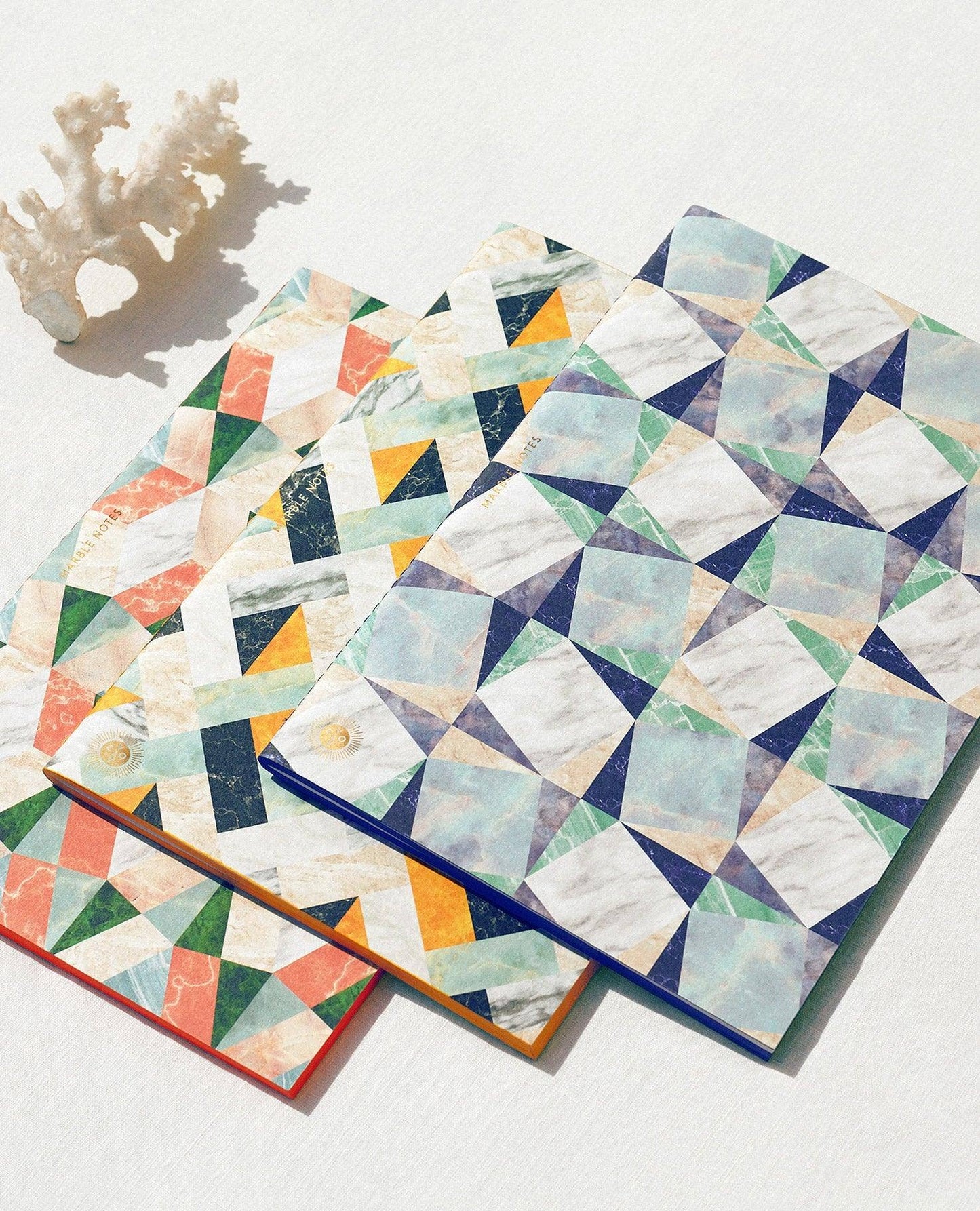 Three geometric-patterned coasters on a white surface with a small coral decoration.