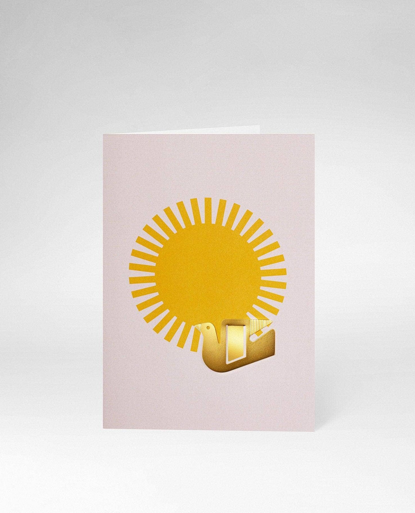 A minimalist greeting card with a pale pink background, featuring a yellow sun graphic and a small gold 3D gift box icon, shown on a light gray background.