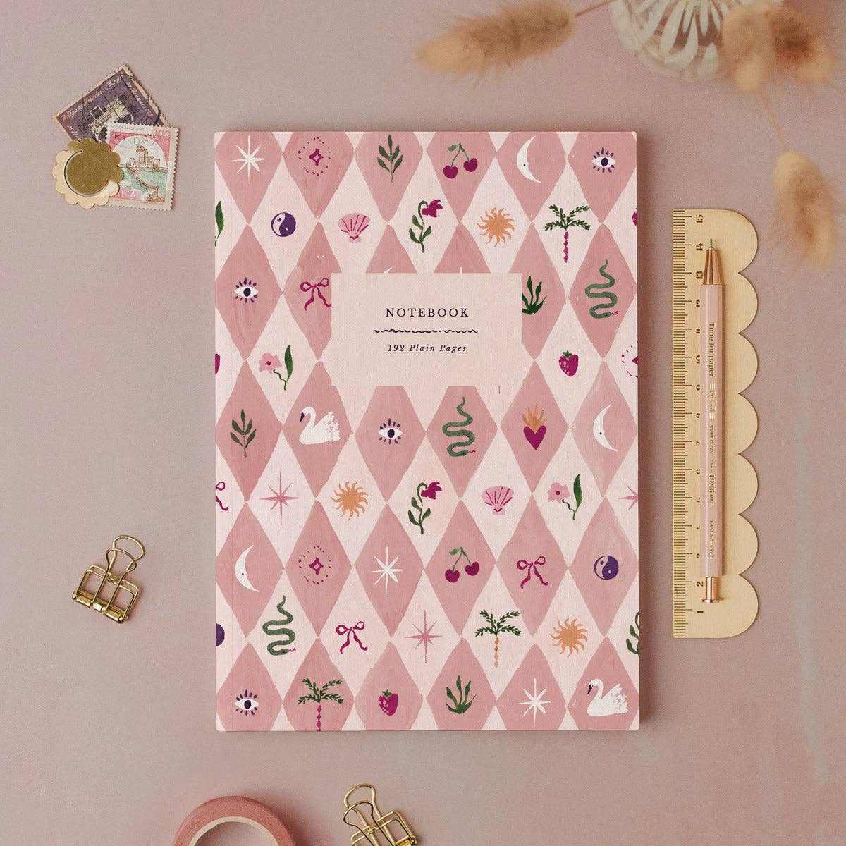 Notebook with decorative cover on a pink background with stationery items.