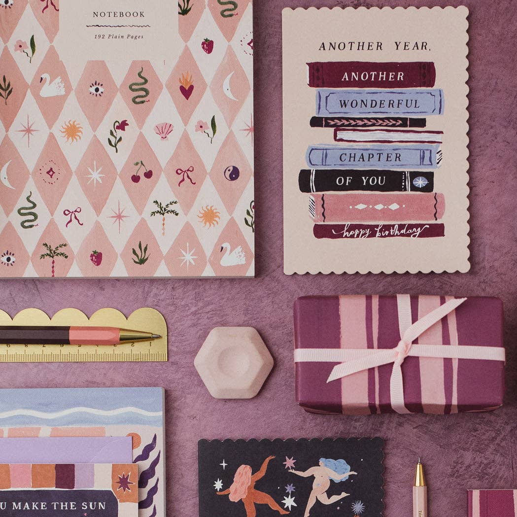 Collection of stationery items including a notebook, cards, and a gift on a purple background