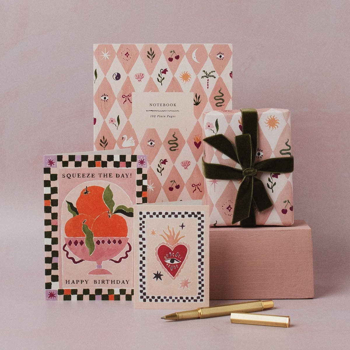 Set of notebooks, cards, and a gift box with a pen on a pink background