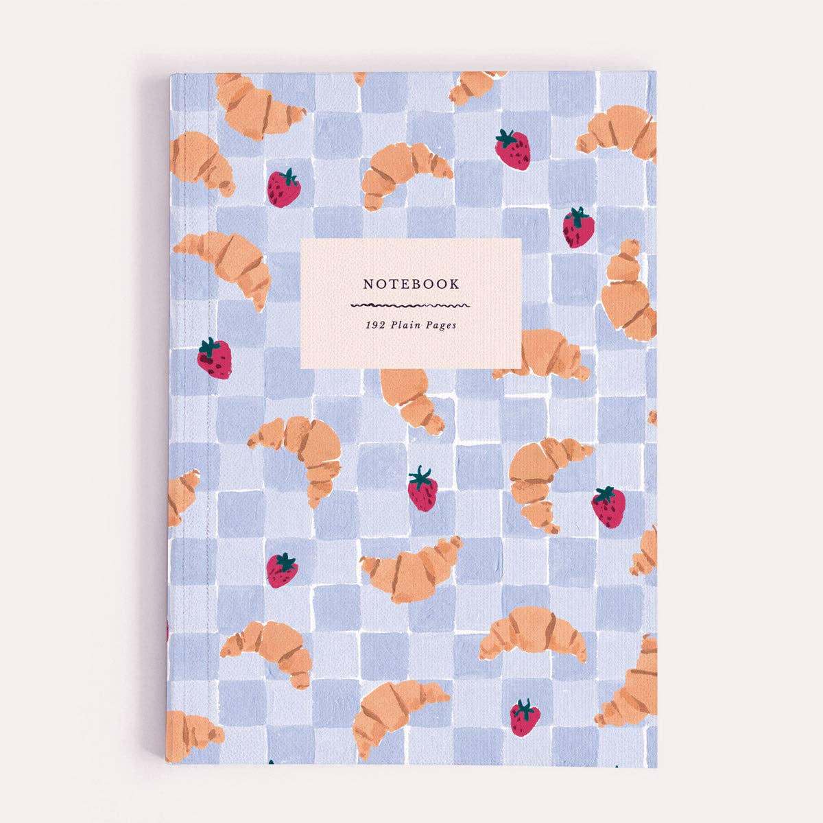 Notebook with a checkered pattern featuring croissants and strawberries on a light blue background.