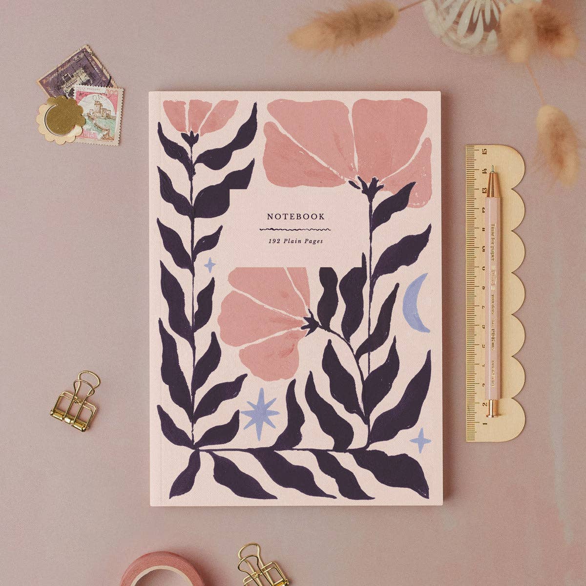 Notebook with floral design on a pink background with stationery items.