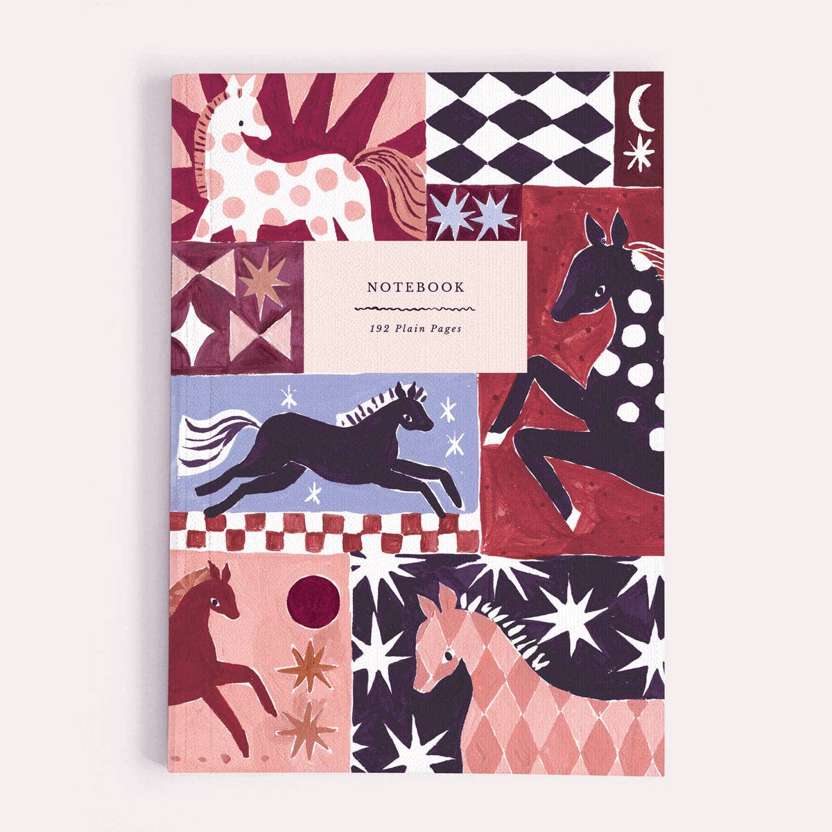A notebook with a whimsical patchwork cover featuring stylized horses, stars, moons, and geometric patterns in pink, red, navy, black, and cream. The center label reads 'NOTEBOOK 192 Plain Pages'.