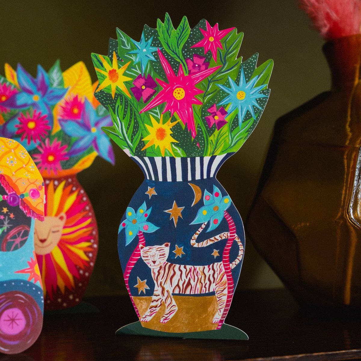 Colorful paper cutout of a vase with flowers and a tiger design on a dark background.
