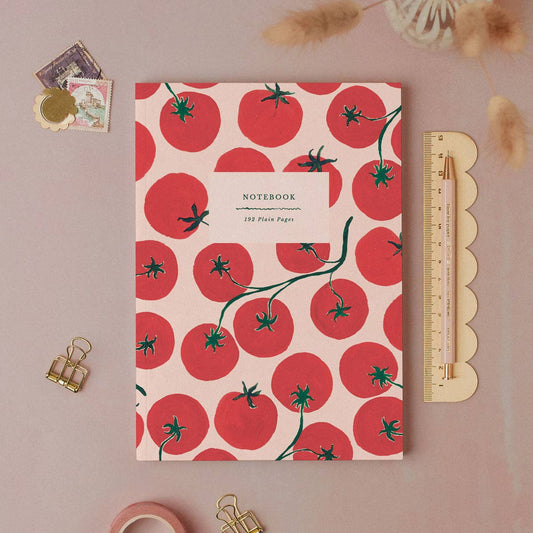 Notebook with red tomato pattern on a pink background, surrounded by stationery items.