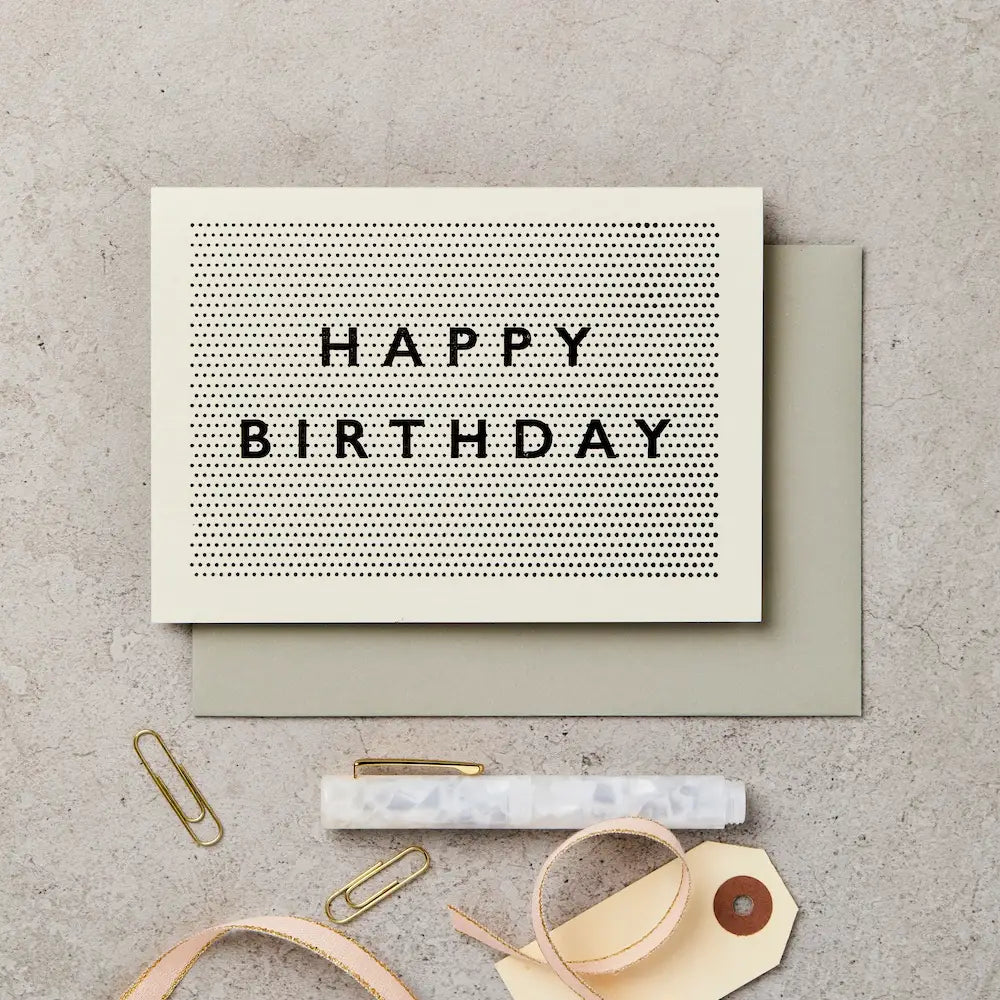 Birthday card with 'Happy Birthday' text on a textured surface with stationery items.