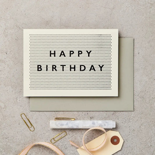 Birthday card with 'Happy Birthday' text on a textured surface with stationery items.