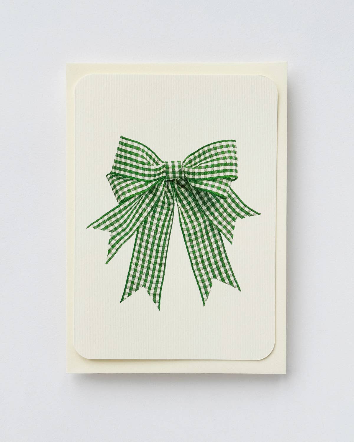 A cream-colored greeting card featuring a green and white gingham checkered ribbon bow printed in the center, shown against a neutral light beige background.