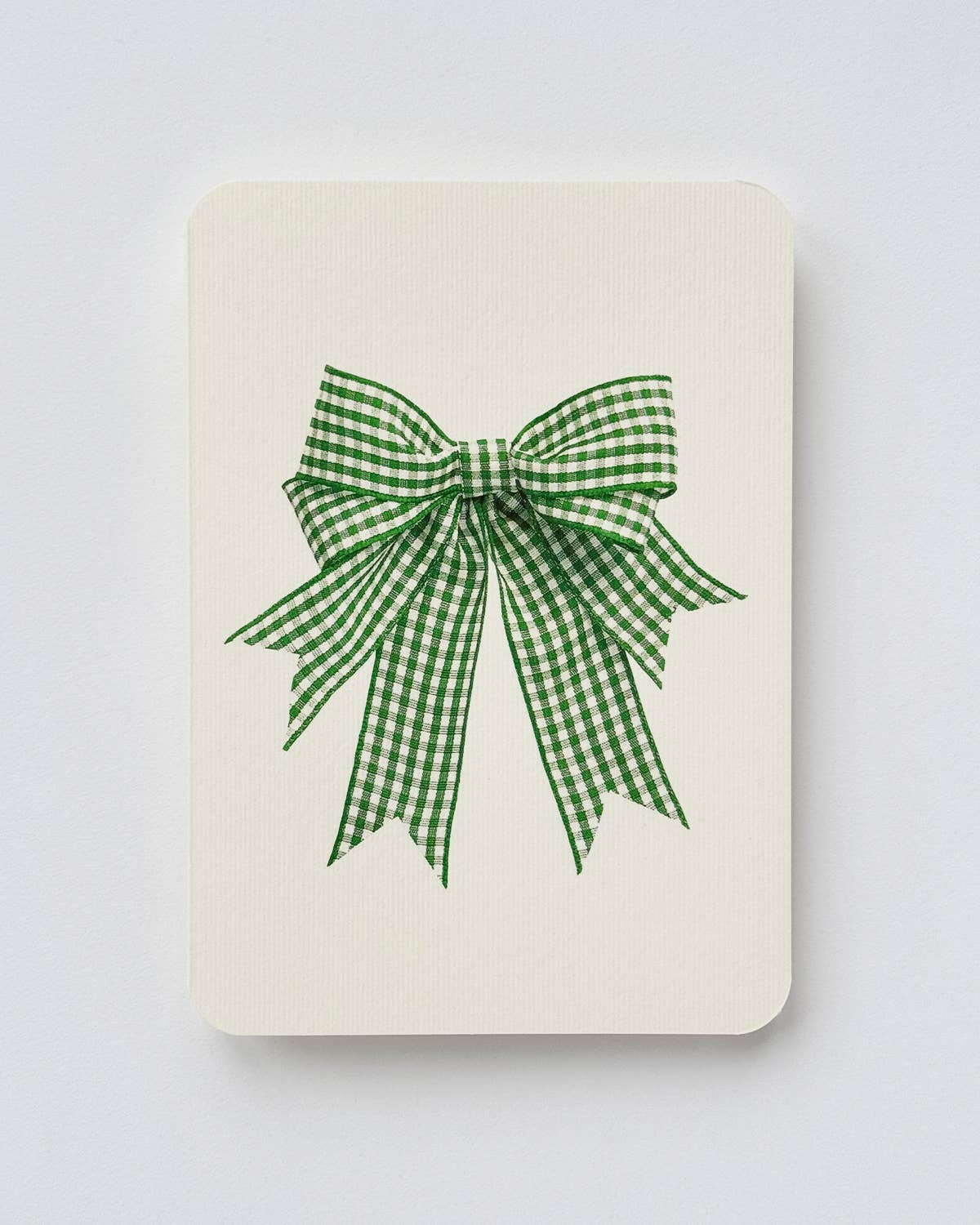 A cream-colored rectangular card or notebook cover featuring a green and white gingham checkered bow design in the center, set against a plain light beige background.