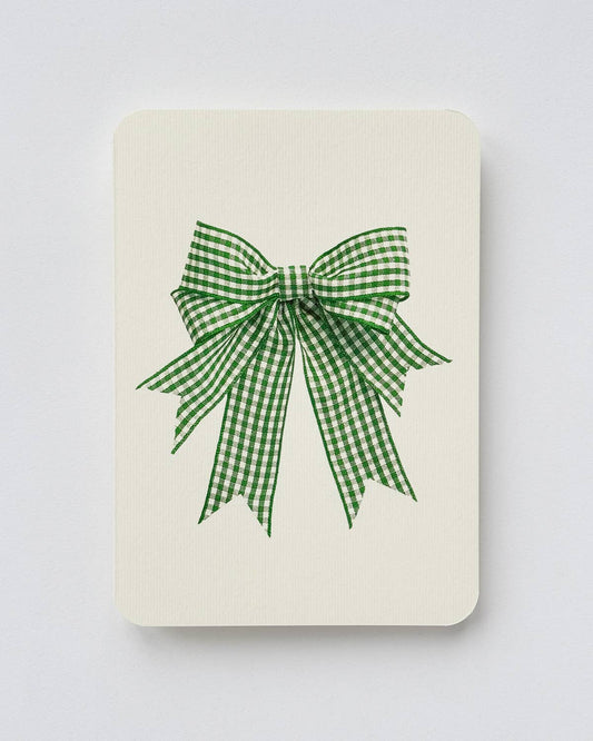 A cream-colored rectangular card or notebook cover featuring a green and white gingham checkered bow design in the center, set against a plain light beige background.